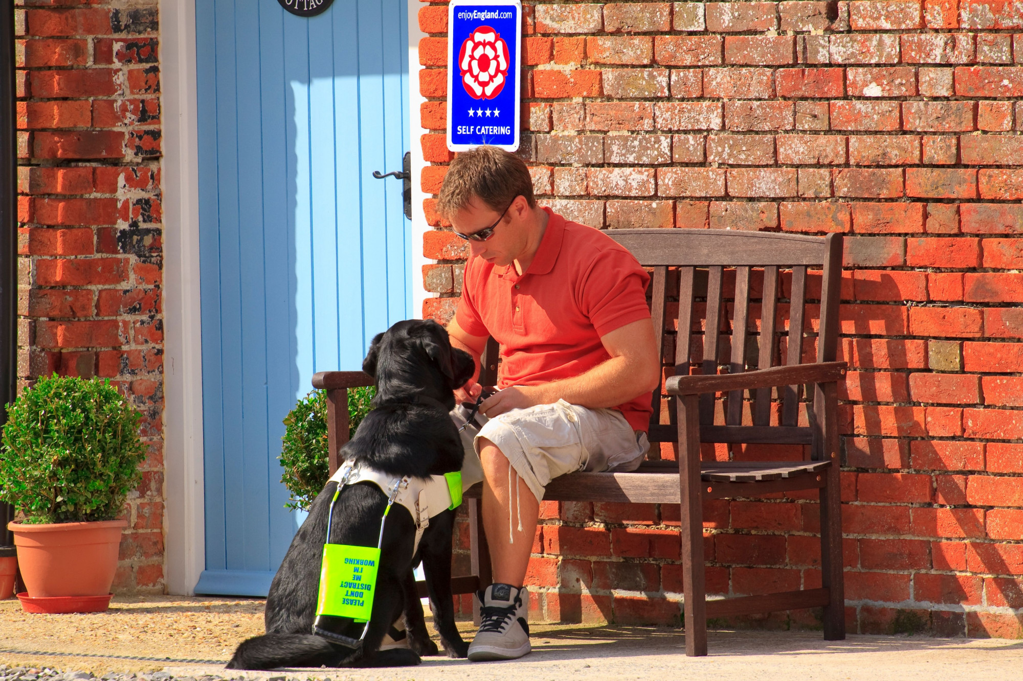 A man with his assistance dog outside his front door at Ellwood Cottages, a set of self catering holiday cottages in rural Dorset. The man is registered blind. Woolland, Dorset, England.