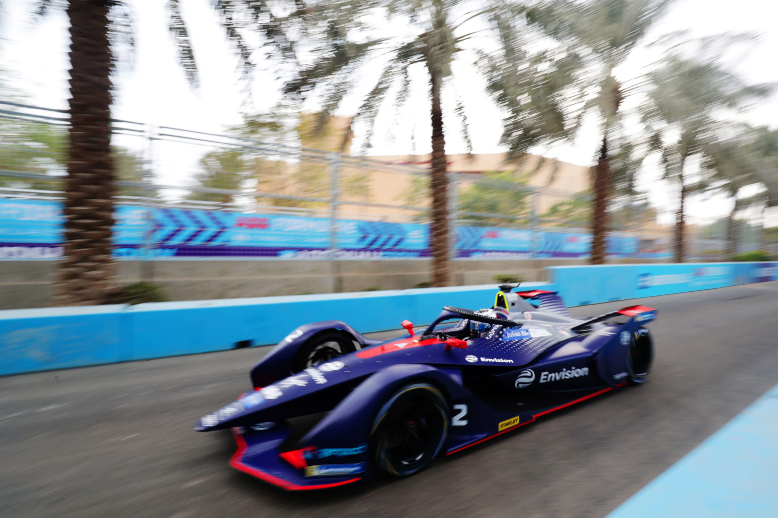 A navy and red racing car speeds down a track lined with blue signage and palm trees.