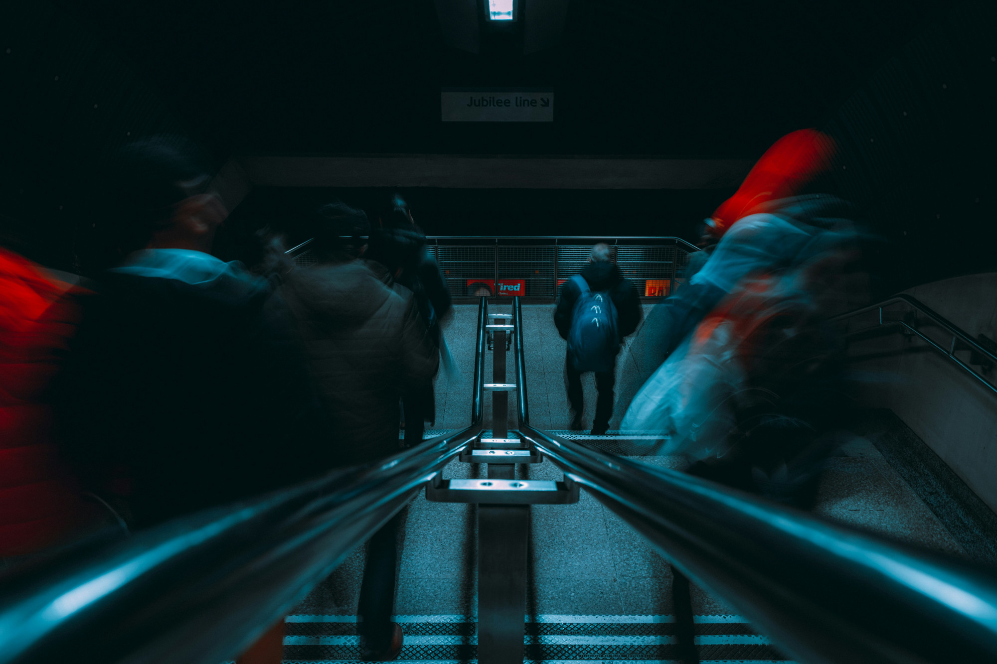 A group of rail passengers move down a dimly-lit stairwell