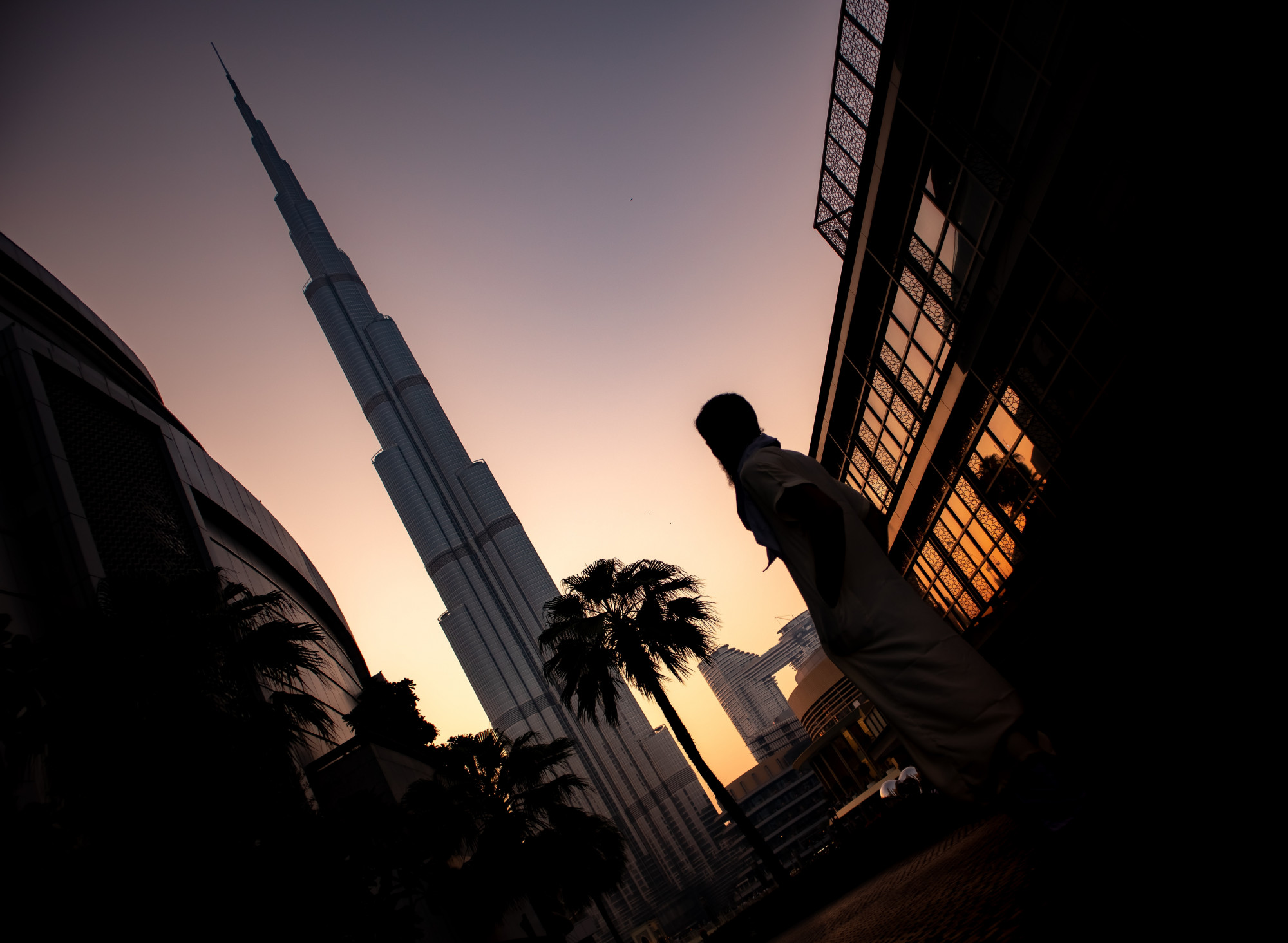 The silouette of a person set against the backdrop of a sunset Middle Eastern skyscraper.