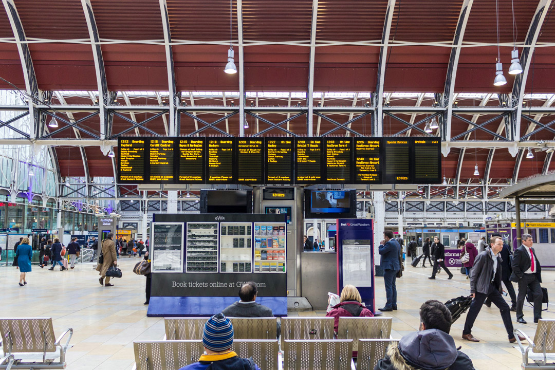 Passengers sit in front of departure boards at a busy railway station