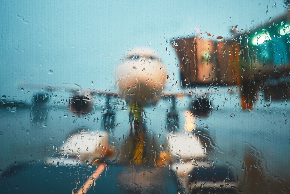 A plane viewed from inside an airport terminal window speckled by rain.