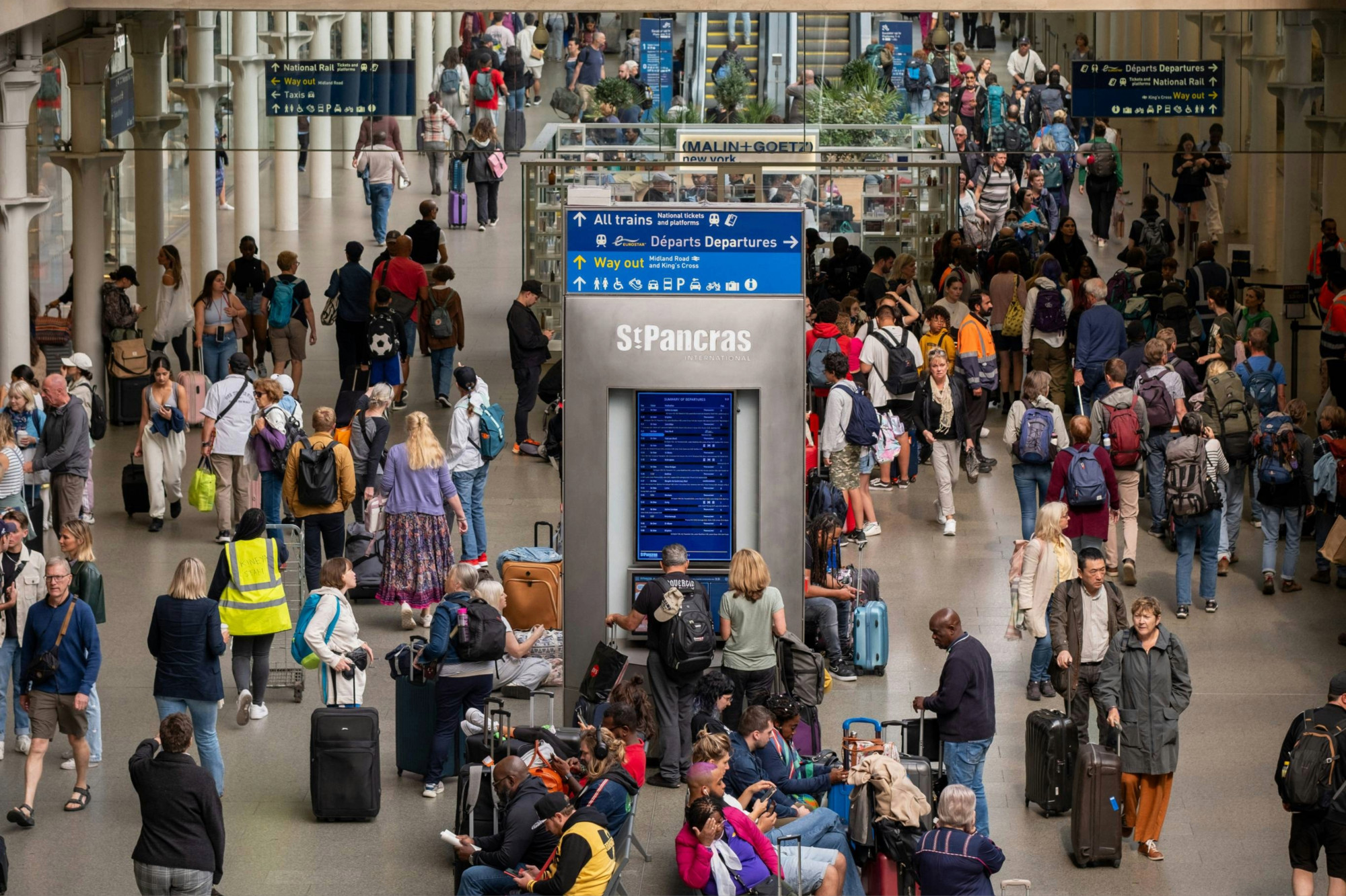 Crowds of travelers move through a busy railway station concourse
