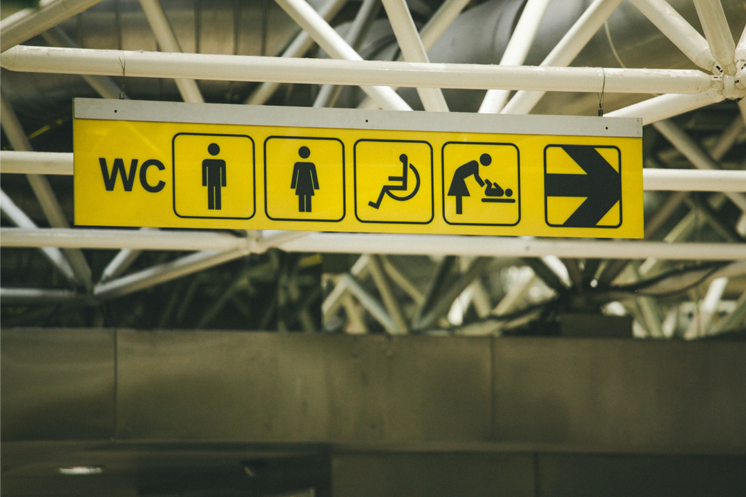 A yellow overhead sign indicates the direction to toilets, including men's, women's, accessible, and baby changing facilities, with a large arrow pointing to the right.