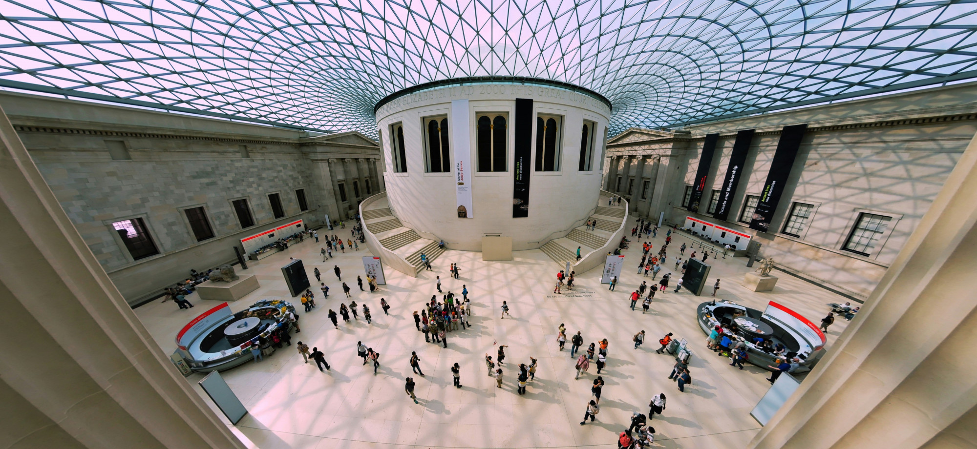 A birds eye photo taken of the main atrium of The British Museum showing information desks, visitors and the distinctive glass roof