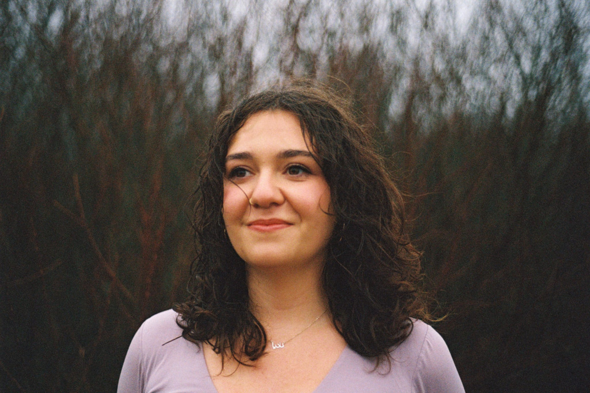 Nadia Malekian, Architect. Nadia has dark brown curly hair, is wearing a light purple top and is standing outside with trees behind her.
