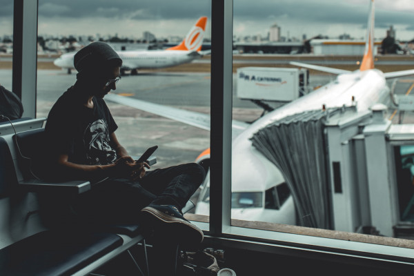 Person sitting in airport departure lounge beside a window. Through the window planes can be seen on the runway.