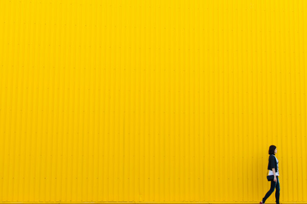 A woman wearing black stands in front of a yellow wall cover image